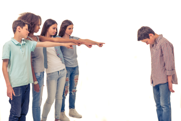 Group of teenage boys and girls is pointing on another boy, who is standing with bent head, isolated on white
